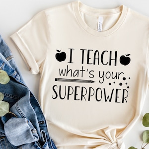 May include: A beige t-shirt with black text that reads "I teach what's your superpower" with a black apple and pencil graphic.