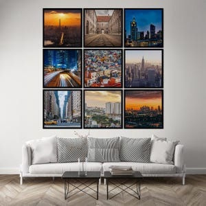 May include: Nine framed city landscape photographs displayed above a white sofa with black and white pillows. The photographs depict various cityscapes, including a sunset over a city, a street scene, and a view of skyscrapers.
