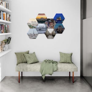 May include: A collection of nine hexagonal wall art pieces featuring cityscapes, displayed above a bench with green cushions and a blanket. The art pieces showcase various city scenes with different lighting and architectural styles.