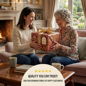 Two women sitting on a couch, one holding a large red gift box with a gold bow, smiling and looking at each other.