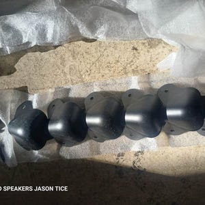 May include: A row of black corner protectors with mounting holes, likely for speaker cabinets, are arranged on a light-colored surface. The text "HEMP-O SPEAKERS JASON TICE" is visible at the bottom.