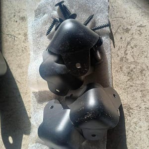 May include: A collection of black corner protectors and screws. The corner protectors are made of a matte black material and have a rounded shape. The screws are black and have a pointed tip. The text "HEMP-O SPEAKERS JASON TICE" is visible.