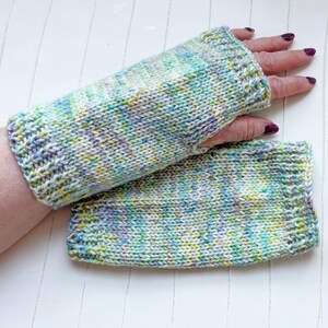 Könnte beinhalten: Ein Paar gestrickte Fingerlose Handschuhe in einem mehrfarbigen Garn mit Schattierungen von Grün, Blau, Lila und Weiß.