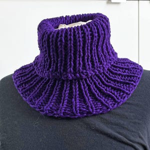 Könnte beinhalten: Ein violetter gestrickter Schalkragen-Halswärmer. Der Schalkragen ist umgeklappt und hat eine gerippte Struktur.