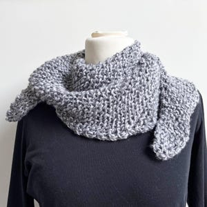 Könnte beinhalten: Ein grauer und weißer gestrickter Schal mit einem strukturierten Muster. Der Schal ist um den Hals einer Schaufensterpuppe gelegt.