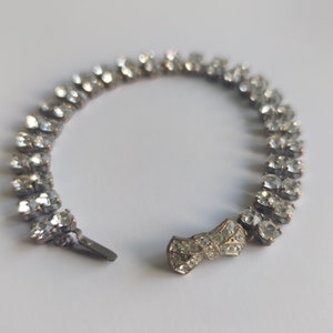 Pode incluir: Uma pulseira de prata com uma fileira de strass transparentes e um fecho em forma de laço.