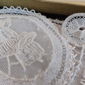 May include: Two white lace doilies, one with a floral design and the other with the word "WALES" embroidered in the center.