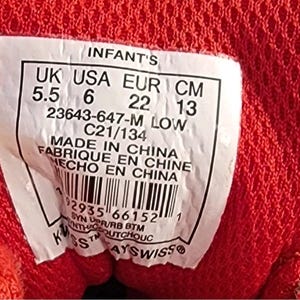 May include: Close-up of a label from a red infant's shoe. The label includes size information: UK 5.5, USA 6, EUR 22, and CM 13. The label also includes the text "MADE IN CHINA" and a barcode.