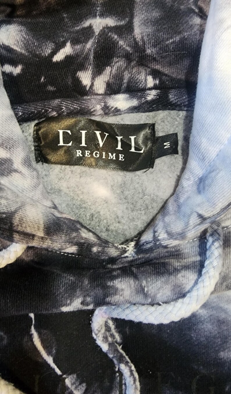 May include: A tie-dye hoodie in shades of black, white, and light blue. The label reads "CIVIL REGIME" in white text on a black background. The hoodie has a drawstring and a medium size tag.