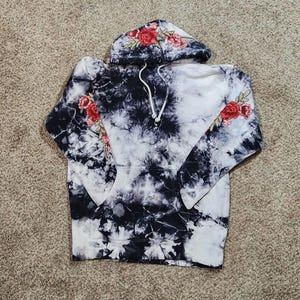 May include: A tie-dye hoodie in black and white with red rose embroidery on the hood and sleeves. The word "ME" is printed on the front. The hoodie has a drawstring and a kangaroo pocket.