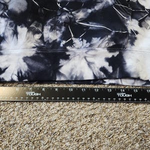 May include: A section of fabric with a tie-dye pattern in shades of black and white. A black ruler is placed along the bottom edge of the fabric, showing measurements in inches.