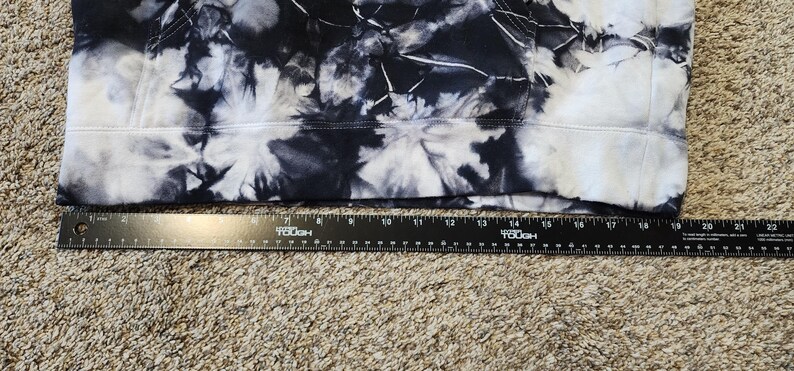 May include: A section of fabric with a tie-dye pattern in shades of black and white. A black ruler is placed along the bottom edge of the fabric, showing measurements in inches.