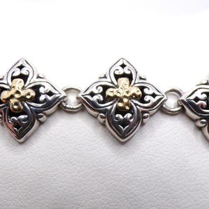 May include: Silver bracelet with gold accents. The bracelet features a series of ornate, diamond-shaped links. Each link has a gold cross in the center and intricate silver filigree detailing. The bracelet is displayed on a white surface.