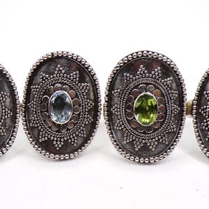 May include: Four silver rings with oval-shaped settings. Each ring features a different colored gemstone: amethyst, aquamarine, peridot, and garnet.