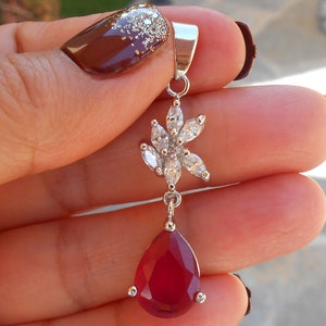 May include: A silver pendant with a red teardrop-shaped gemstone and a flower design with clear cubic zirconia stones.