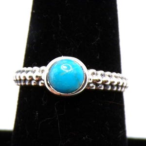 May include: A silver ring with a turquoise stone set in a beaded band.