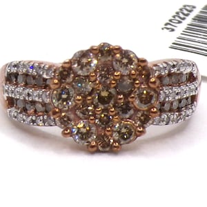 May include: A rose gold ring with a cluster of champagne diamonds in the center and a band of smaller diamonds. The ring is on a white surface with a tag that says "Made in India" and a barcode.