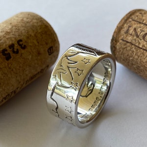 May include: A silver ring with an engraved design of stars and a bird. The ring is next to two corks. The ring has the words "GOLDEN STATE" engraved on it.