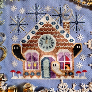 May include: Cross-stitch design of a gingerbread house with a clock face, ghosts, and snowflakes on a light blue background. The house features brown, white, and purple details, with red accents. The design is surrounded by decorative elements.