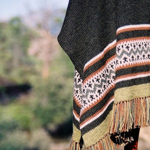 Puede incluir: Un poncho de punto negro y verde con un patrón geométrico y flecos.