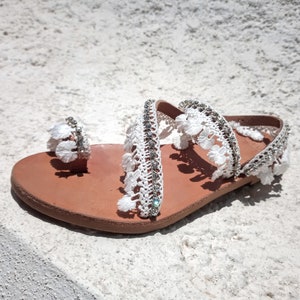 White leather sandals with white crocheted straps and rhinestones. The sandals have a brown leather sole.