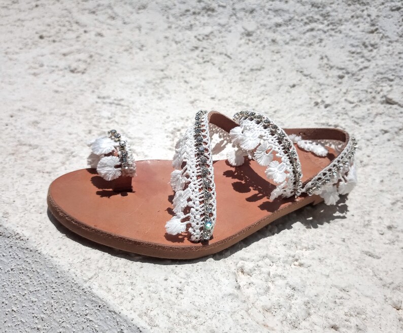 White leather sandals with white crocheted straps and rhinestones. The sandals have a brown leather sole.