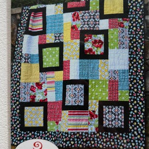 May include: A quilt pattern booklet titled Perfect Ten #SGD006 by Swirly Girls. The cover features a colorful patchwork quilt with various floral, polka dot, and striped fabric squares framed by black borders, all enclosed in a clear plastic sleeve.