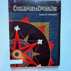May include: A book titled "Precision & Panache" with a colorful quilt design on the cover. The cover features a dark background with a starburst pattern in red, black, and gold. The author's name, Susan K Cleveland, is also visible.