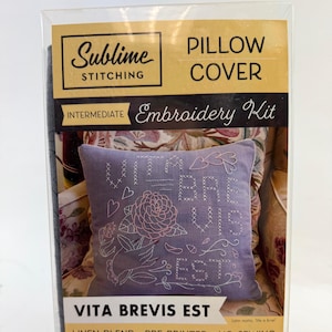 May include: A pillow cover embroidery kit with the text "VITA BREVIS EST" in white thread on a lavender pillow. The kit includes a 16" x 16" linen blend pillow cover, pre-printed design, and 7 colors of floss. The packaging reads "Sublime Stitching".