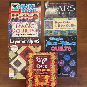 May include: A collection of quilting books with colorful covers. Titles include "Square Magic Quilts," "Stars A La Carte," "Magic Quilts By The Slice," "Layer 'em Up #2," "Magic Stack-n-Whack Quilts," and "Stack the Deck Revisited."