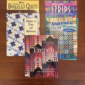 May include: A collection of quilting books, including "Bargello Quilts," "Super Simple Strips," "Another Can of Worms," and "French Braid Quilts." The books feature colorful quilt designs and patterns. The book "Open a Can of Worms" is also visible.