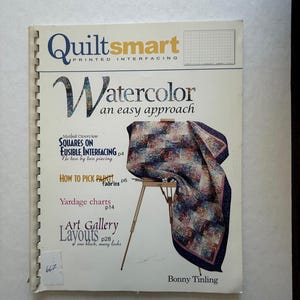 May include: A spiral-bound book titled "Quiltsmart" with the subtitle "Watercolor an easy approach." The cover features a colorful quilt draped over a wooden easel. Text includes "Squares on Fusible Interfacing" and "Art Gallery Layouts."