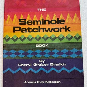May include: A vintage book titled "The Seminole Patchwork Book" by Cheryl Greider Bradkin. The cover features a colorful geometric design in shades of red, orange, yellow, green, blue, and purple. Published by A Yours Truly Publication.