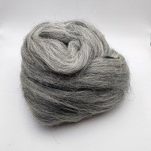May include: A close-up of a clump of gray wool roving. The wool is soft and fluffy, and it is perfect for felting or spinning.