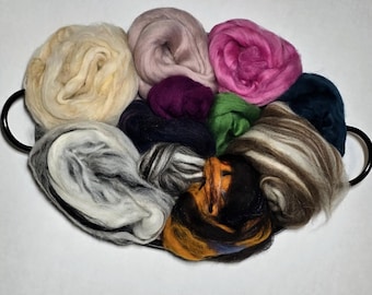 May include: A collection of colorful wool roving in a black handled tray. The wool is in various shades of cream, pink, purple, green, and brown. The tray is oval-shaped and has two black handles.