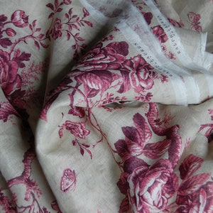 May include: A close-up of a fabric with a floral pattern. The fabric is a light beige color with a pink and white floral design. The fabric is folded in half, and the floral pattern is visible on both sides.