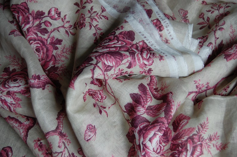 May include: A close-up of a fabric with a floral pattern. The fabric is a light beige color with a pink and white floral design. The fabric is folded in half, and the floral pattern is visible on both sides.