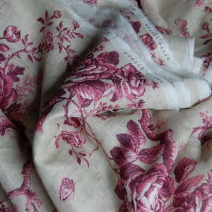May include: A close-up of a beige linen fabric with a pink floral pattern. The fabric is folded and has a white label with the text "RALPH LAUREN" on it.