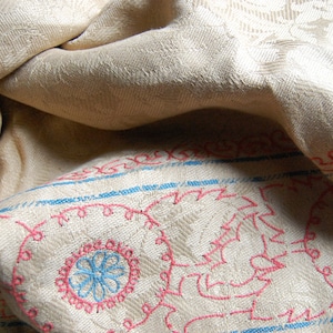 Puede incluir: Primer plano de una tela blanca con un dise&ntilde;o bordado en azul y rosa. La tela est&aacute; doblada y tiene una superficie texturizada.