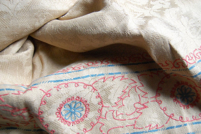 Puede incluir: Primer plano de una tela blanca con un dise&ntilde;o bordado en azul y rosa. La tela est&aacute; doblada y tiene una superficie texturizada.