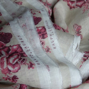May include: A white fabric with a pink floral pattern and the text "RALPH LAUREN" repeated on the fabric.