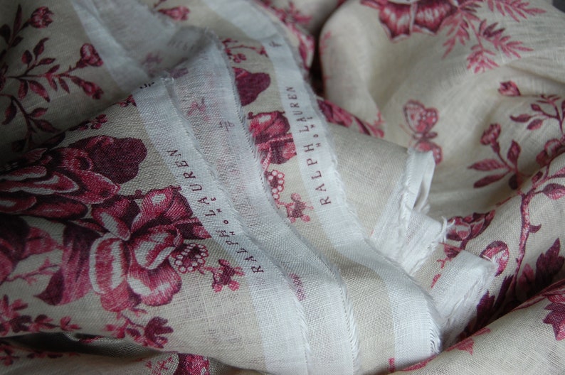 May include: A white fabric with a pink floral pattern and the text "RALPH LAUREN" repeated on the fabric.