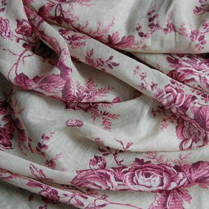 May include: A close-up of a white fabric with a pink floral pattern. The fabric is wrinkled and has a soft, textured look.