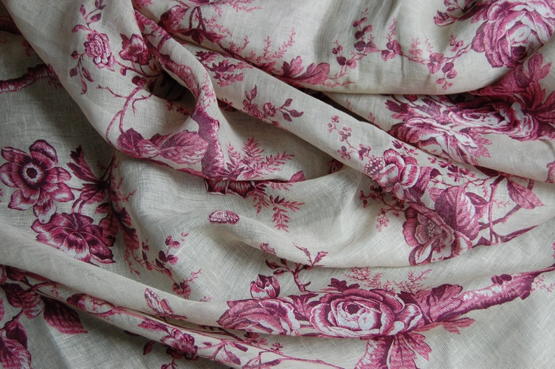 May include: A close-up of a white fabric with a pink floral pattern. The fabric is wrinkled and has a soft, textured look.