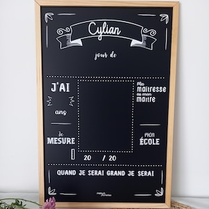 Op de afbeelding: Een rechthoekig krijtbord met een lichthouten lijst en witte opdruk. Het bord bevat secties voor een naam, leeftijd, school, lengte en toekomstige beroepsdoelen, met een centrale rechthoekige ruimte voor een foto.