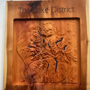 Könnte beinhalten: Ein Wandkunstwerk aus Holz mit einer geschnitzten Karte des Lake District. Die Karte ist von einem Holzrahmen umgeben und die Worte "The Lake District" sind oben eingraviert.