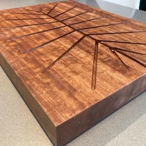 Op de afbeelding: Een rechthoekig houten muziekinstrument met een donkerbruine afwerking. De bovenkant heeft uitgesneden lijnen in een boomachtig patroon. Het instrument staat op een lichtgekleurd oppervlak.