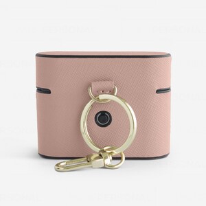 May include: A dusty pink textured protective case for wireless earbuds featuring a gold-toned metal ring and a matching gold-toned lobster clasp attachment. The case has a black trim along the edges and a small circular black button on the front.