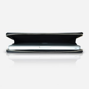 May include: A black laptop sleeve with a metallic zip closure, partially open to reveal a silver laptop inside. The sleeve is rectangular and features a slim profile, designed to securely hold and protect a portable computer during transport.