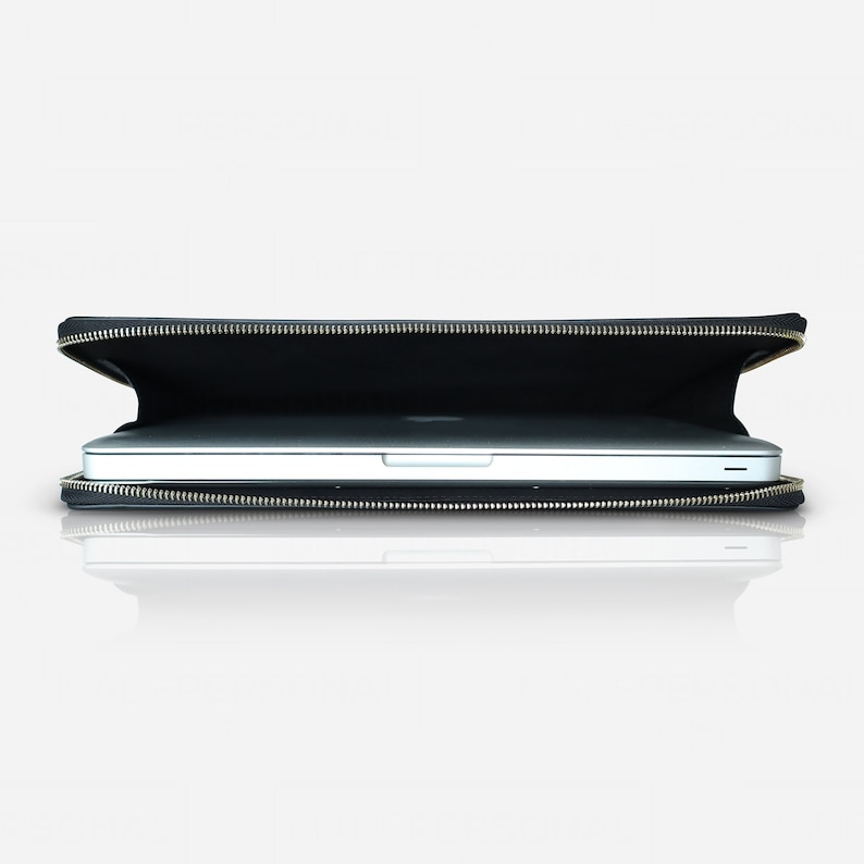 May include: A black laptop sleeve with a metallic zip closure, partially open to reveal a silver laptop inside. The sleeve is rectangular and features a slim profile, designed to securely hold and protect a portable computer during transport.